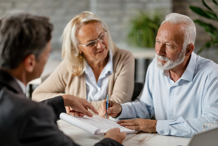 Attractive older couple signing a document in front of someone wearing a business suit, Image shared to support the fact that our Braintree estate planning law firm helps you the right documents in place for an effective estate plan, such as a last will and testament document.
