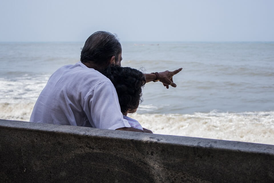 This is the image of the backs of a grandfather or father and a teenage granddaughter or daughter. The two are seated on a bench looking out at the ocean and the surf and the man is pointing at the ocean. This image is shown in conjunction with our Braintree MA estate planning law firm's blog post about guardianship.

