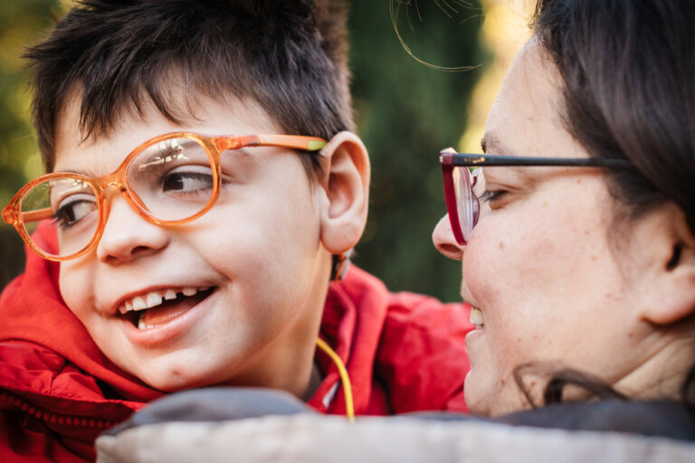 Child With Special Needs In His Mother's Arms. They both are smiling and looking happy. The child is wearing bright orange glasses. This image is shown in connection with our estate planning law firm's blog post about special needs planning.